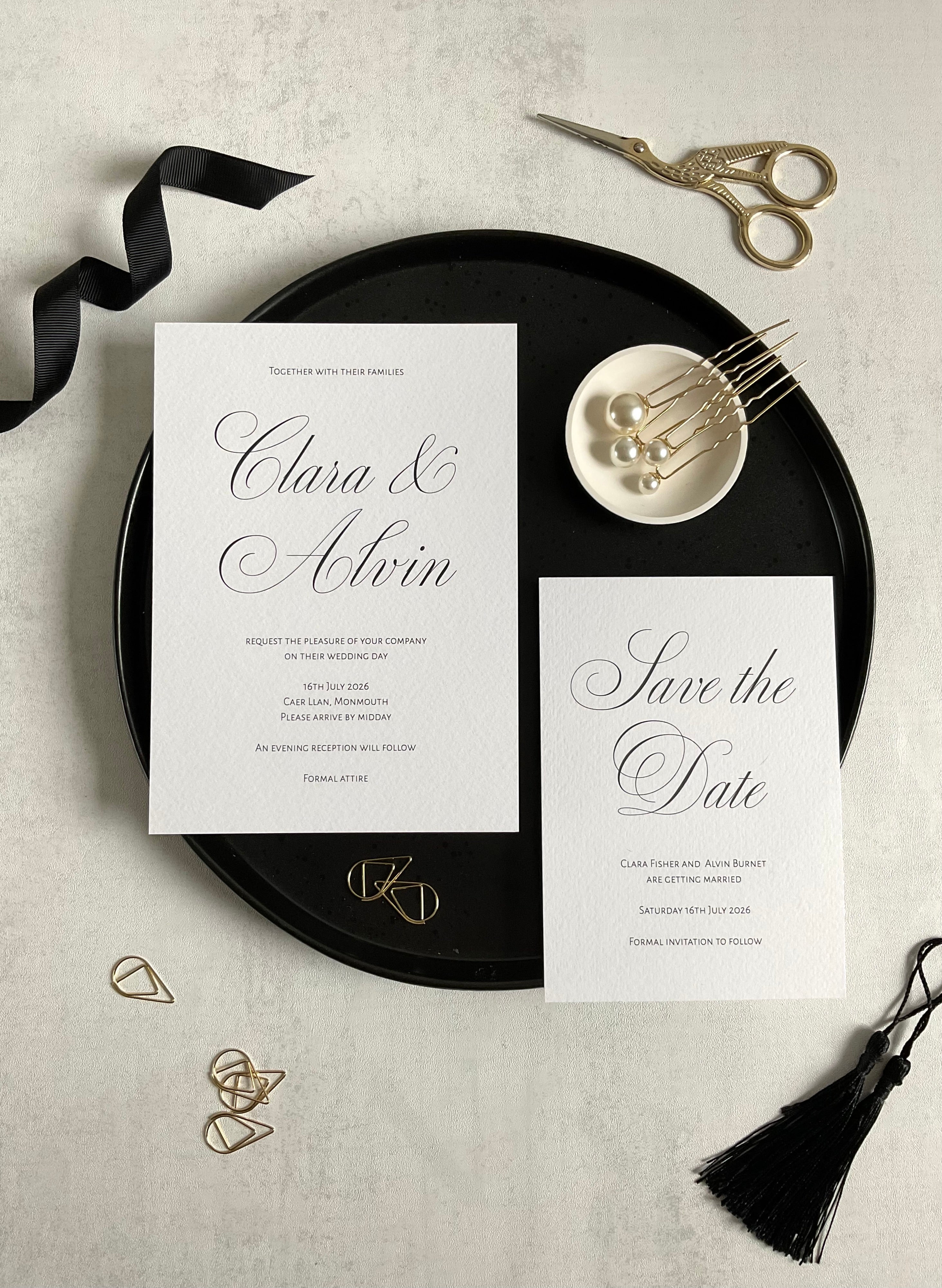 Black and white wedding invitation and save the date card, pictured on a black charger plate to contract the white invitation. Titles have calligraphic font and the rest of the type is sans serif.