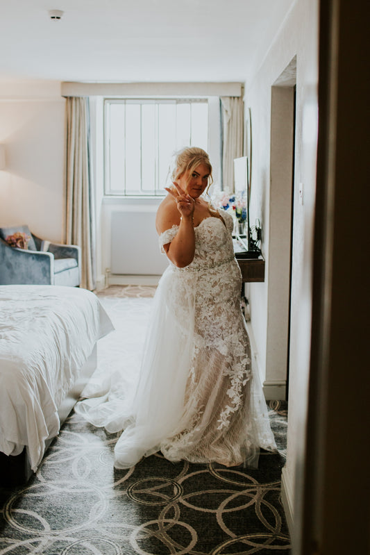 Bride getting ready on wedding day in lace white wedding dress and making the peace sign with her hand